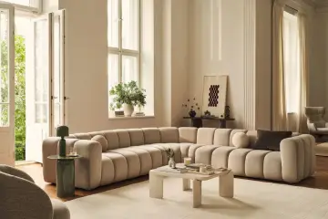 Ampio divano componibile color crema, dalle forme morbide e arrotondate, perfetto per definire le dimensioni di un salotto moderno.