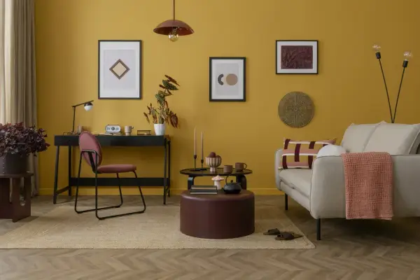 Un salotto con pareti giallo ocra e dettagli tortora. Un divano beige, un pouf tortora e un tappeto in juta creano un'atmosfera accogliente.