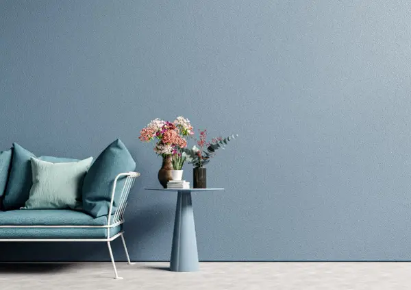 Divano blu e tavolino con fiori su muro azzurro, ispirazione per tecniche di pittura pareti moderne.
