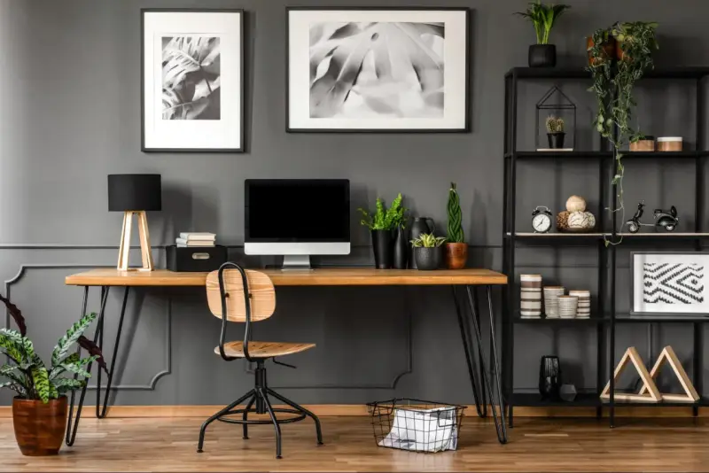 Arredamento studio casa: scrivania in legno con computer, sedia, piante e libreria nera piena di oggetti decorativi.