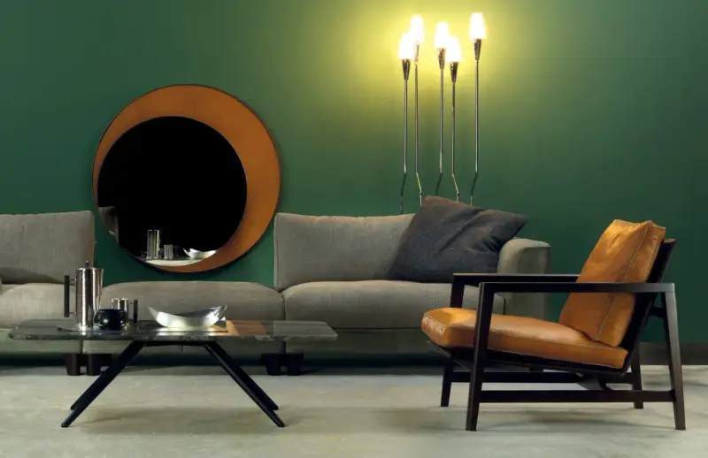 Elegante soggiorno con divano grigio, poltrona in pelle color cuoio e specchio rotondo. Idee su come abbinare divano e poltrone diverse.
